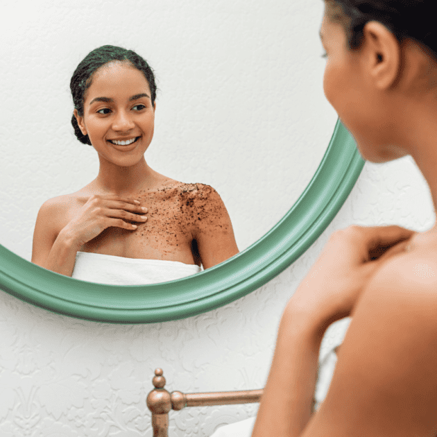 A black woman looking in a mirror rubbing a natural srub on herself