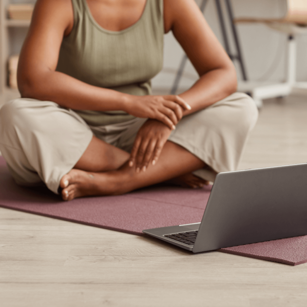a woman of color watching an online yoga class and sitting on a yoga mat