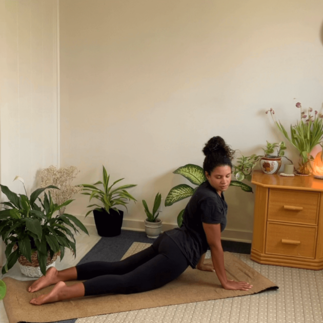 A black woman doing an upward facing dog on her yoga mat at home.
