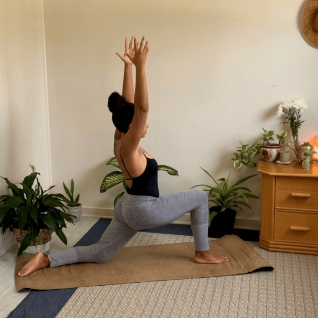 A mixed black woman doing a low lunge in her room during her yoga practice.