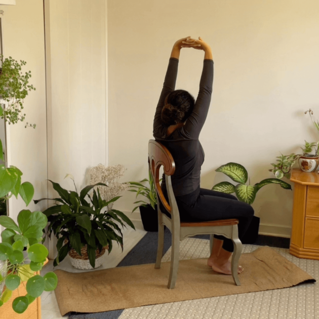 a black woman doing chair yoga in her home during her home yoga practice