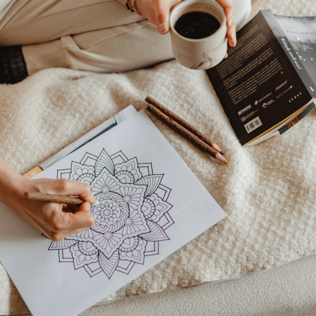 a teen coloring in a mandala coloring sheet with a book and cup of tea
