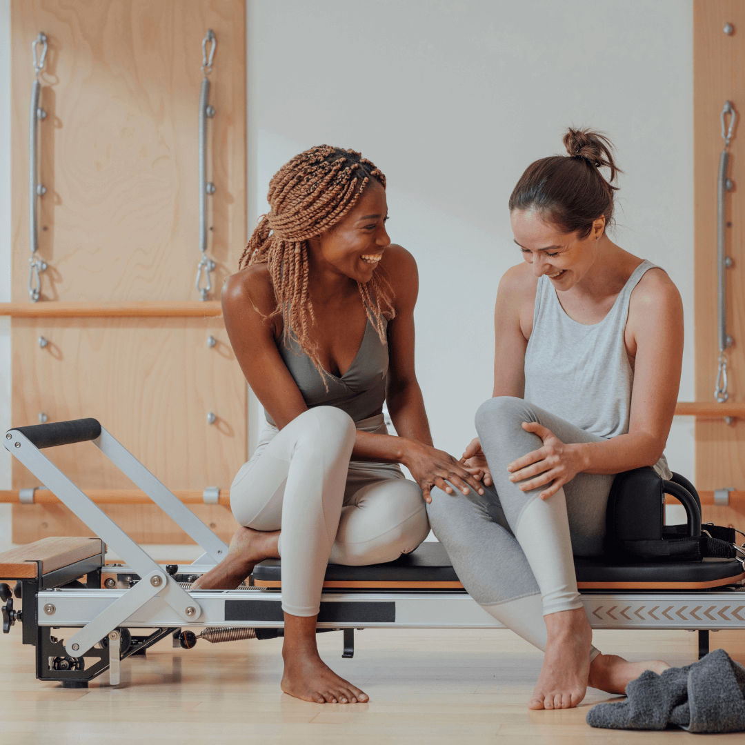 two women sitting on a pilates reformer