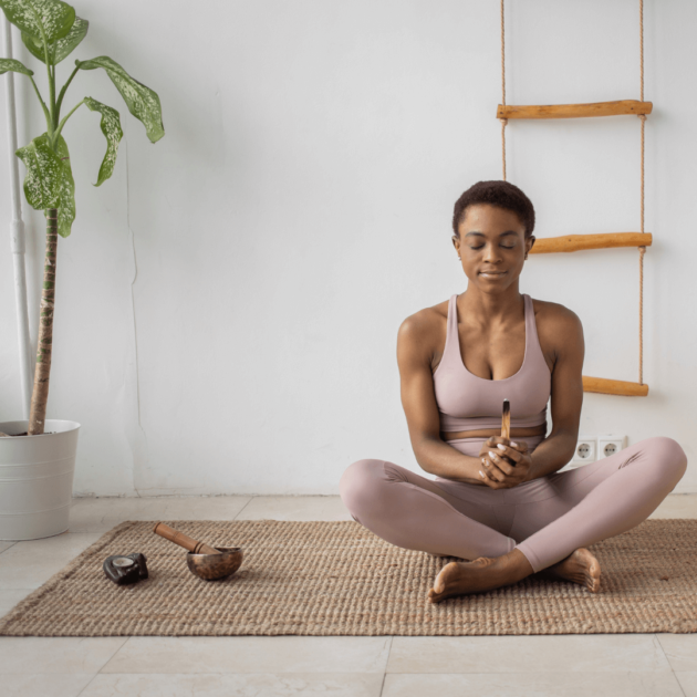 a woman sitting in meditation on her yoga rug in her minimalist yoga room.